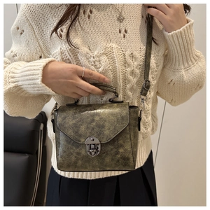 Gros plan du sac bandoulière vintage vert olive avec fermoir bronze sur un pull