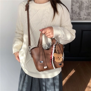 Brown leather tote bag with bear charm and adjustable strap worn on cream knit sweater