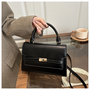 Close-up of a black glossy crossbody bag with golden clasp in a cafe setting