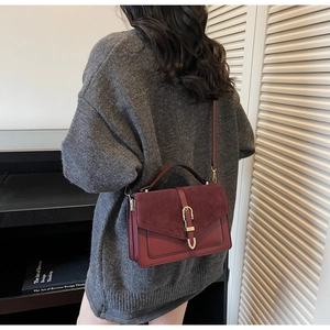 Detail of burgundy shoulder bag featuring suede flap and metallic buckle on model