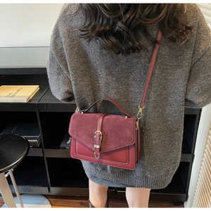 Detail of burgundy crossbody bag with matte suede texture and gold buckle accents