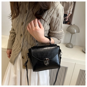 Mannequin portant un sac bandoulière vintage noir avec fermoir argenté dans un salon