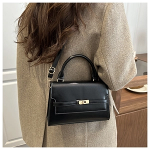 Detail of black crossbody bag with gold lock and top handle on a wool coat