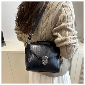 Sac bandoulière rétro noir à texture plissée, porté à l'épaule dans un intérieur chic