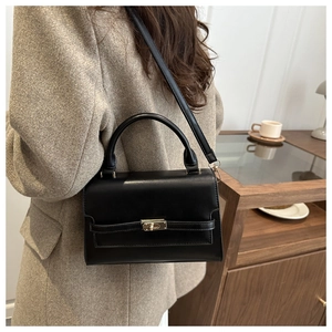 Detail of black trapezoid handbag in matte leather with gold clasp on brown wool coat
