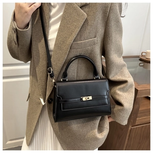 Detail of black leather handbag with gold twist lock and rigid curved top handle