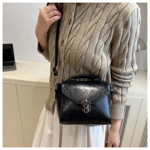 Détail d'un petit sac carré en cuir noir brillant avec fermoir tournant et anse supérieure