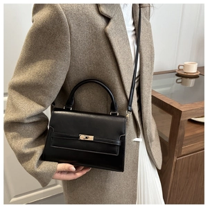 Close-up of black leather mini square bag with golden hardware lock and leather straps