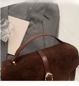 Detail of dark brown suede handbag featuring reinforced leather handle and gold hardware