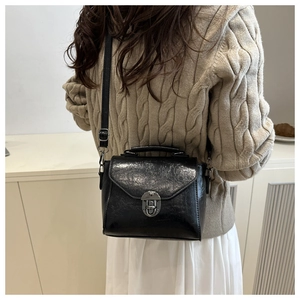 Détail d'un sac bandoulière en cuir texturé noir porté avec un pull en maille beige clair