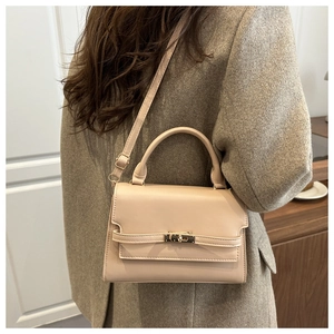 Detail of minimalist beige leather crossbody bag with metal lock and handle on model
