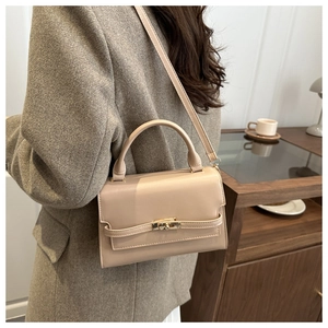 Chic beige crossbody bag with gold lock buckle shown on model in a modern interior setting