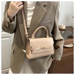 Detail of elegant beige crossbody bag featuring metal turn-lock and top handle on model