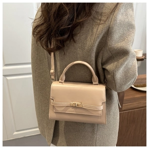 Detail of beige leather handbag with gold twist lock and adjustable shoulder strap worn by model