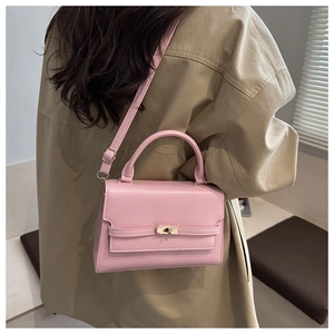 Detail of pink leather handbag with gold metal clasp shown on person in khaki trench coat