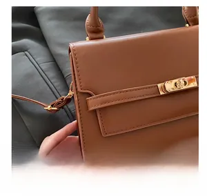 Detail of brown leather handbag with gold metal twist lock and decorative belt strap