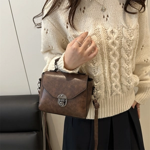Sac à bandoulière marron rétro avec fermoir rotatif argenté et sangle porté par un modèle