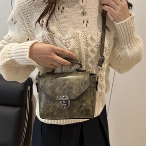 Sac bandoulière rétro bronze avec finition métallique et fermoir métal sur tricot beige