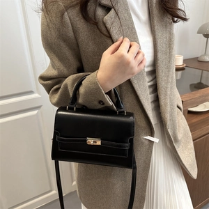 Elegant black leather handbag with gold metal lock buckle worn by a model in a casual setting