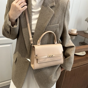 Elegant beige crossbody bag with gold hardware shown on a model in a brown suit