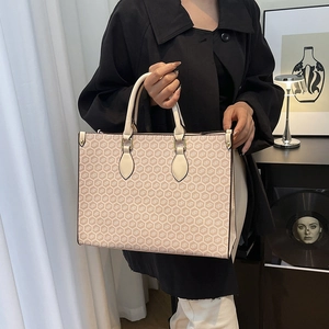 Elegant ivory tote bag with geometric pattern and leather handles held by a model