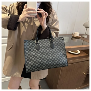Detail of grey tote bag with M-letter monogram pattern and black leather handles