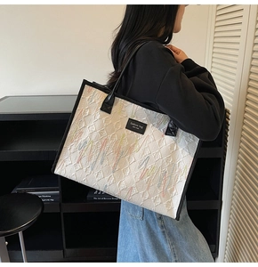 Detail of white tote bag with colorful embroidery patterns and black leather handles