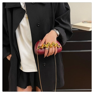 Detail of burgundy leather clutch featuring a designer wavy gold metal handle and chain