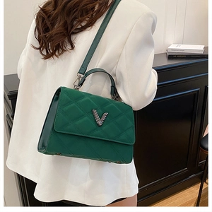 Détail d'un sac à main matelassé vert foncé avec logo V argenté porté par un mannequin en blanc