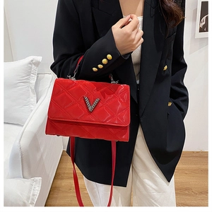 Détail d'un sac à main matelassé rouge avec logo V en métal et poignée sur blazer noir