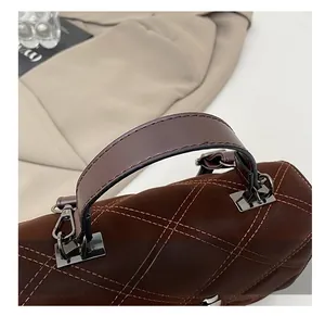 Détail du sac à main en cuir matelassé marron foncé montrant les poignées et le métal brillant