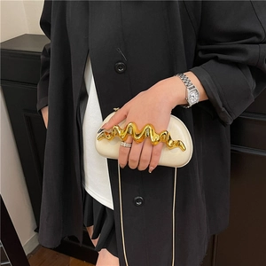 Chic beige clutch bag with wavy gold handle and chain strap on a black trench coat