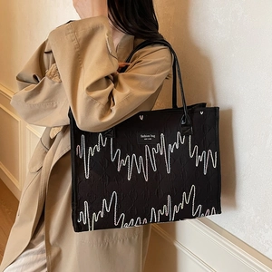 Sac fourre-tout noir texturé avec broderie vagues porté par un mannequin en trench