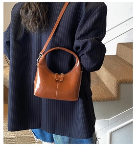 Borsa a mano in pelle verniciata marrone abbinata a un blazer blu scuro su modella