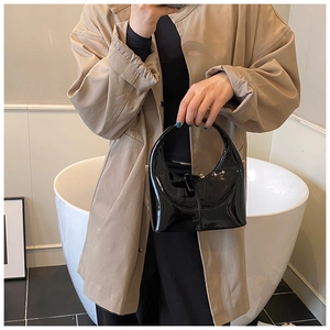 Dettaglio della borsa a mezzaluna in vernice nera lucida con un trench coat kaki
