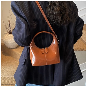 Borsa a tracolla lucida marrone caramello indossata su un blazer blu navy scuro