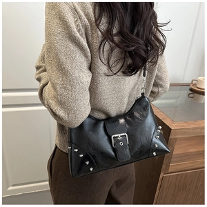Detail of black crossbody bag with silver buckle and studs on model's shoulder