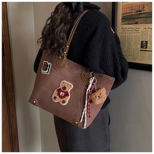 Detail einer braunen Tragetasche mit Bärenstickerei und Plüschanhänger im Retro-Stil
