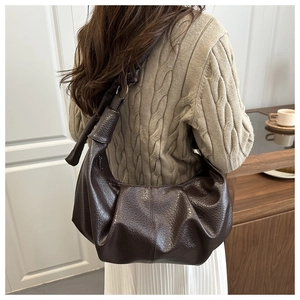 Detail of dark brown leather crossbody bag with pleated cloud shape and knotted strap