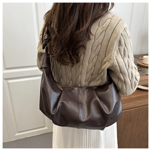 Detail of dark brown leather pleated dumpling bag with knot shoulder strap on model
