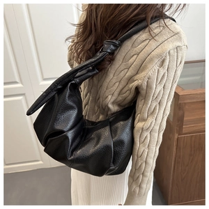 Detail view of black dumpling shoulder bag featuring ruched faux leather and knotted strap