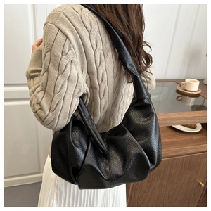 Detail of black pleated faux leather hobo bag showing shoulder strap knot and soft texture
