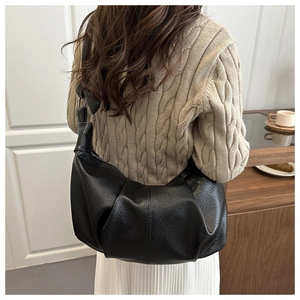 Detail of black pleated faux leather hobo bag worn with a knit sweater for casual style