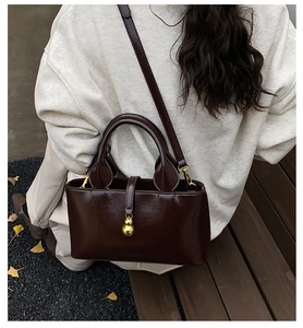 Close-up of vintage dark brown faux leather handbag with gold gourd charm on wooden bench