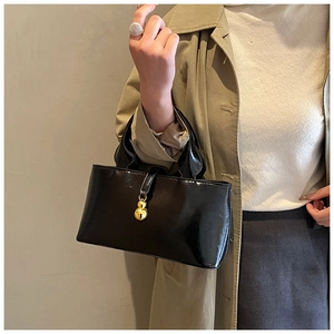 Detail of a black patent leather handbag with a unique gold metal gourd-shaped clasp