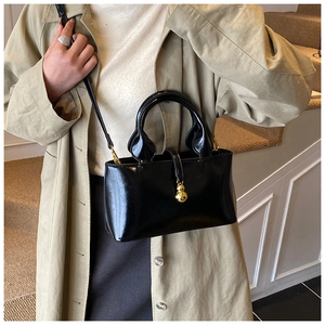 Close-up of black patent leather crossbody bag with golden gourd pendant detail