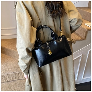 Detail of glossy black patent leather handbag with a unique gold gourd-shaped charm