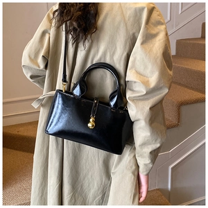 Detail of glossy black patent leather bucket bag with gold hardware on a beige coat