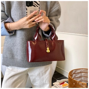 Detail of burgundy patent leather handbag with gold gourd ornament and wavy handle