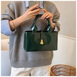 Detail of dark green patent leather handbag with a gold gourd-shaped buckle